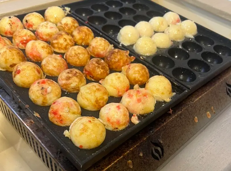 Takoyaki balls browning on the hot griddle, a few still pale