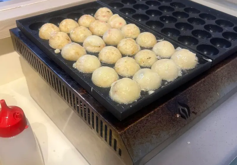 Takoyaki batter setting in the griddle, still pale