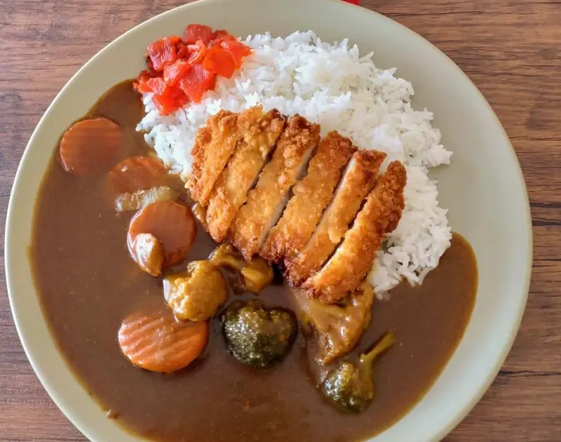 A plate of katsu curry with rice and red pickles