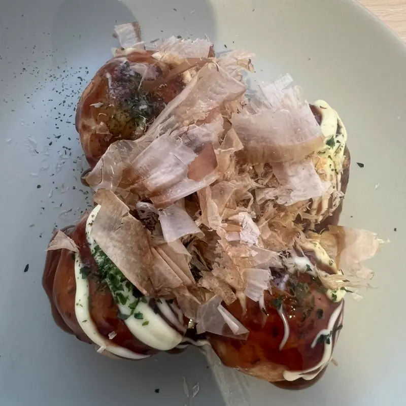 Takoyaki on a grey plate with mayo, sauce and a pile of bonito flakes